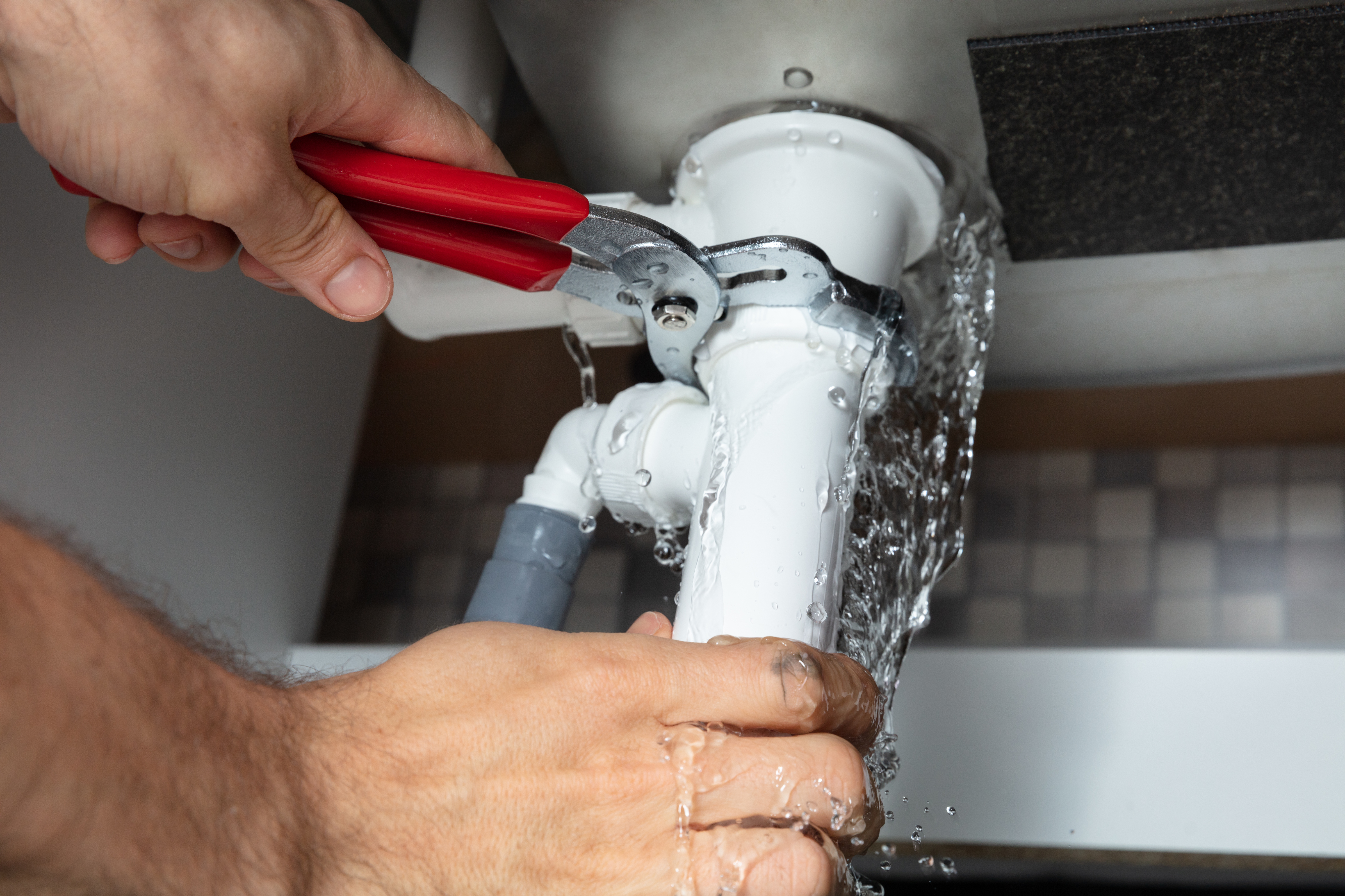 Close-up of male plumber fixing white sink pipe with adjustable wrench
